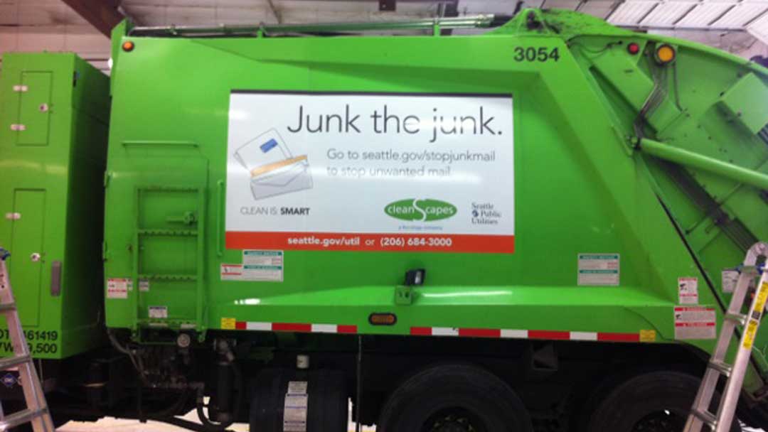 Large vinyl banner attached to side of waste disposal truck reading 'Junk the Junk.' with illustration of junk mail envelopes.